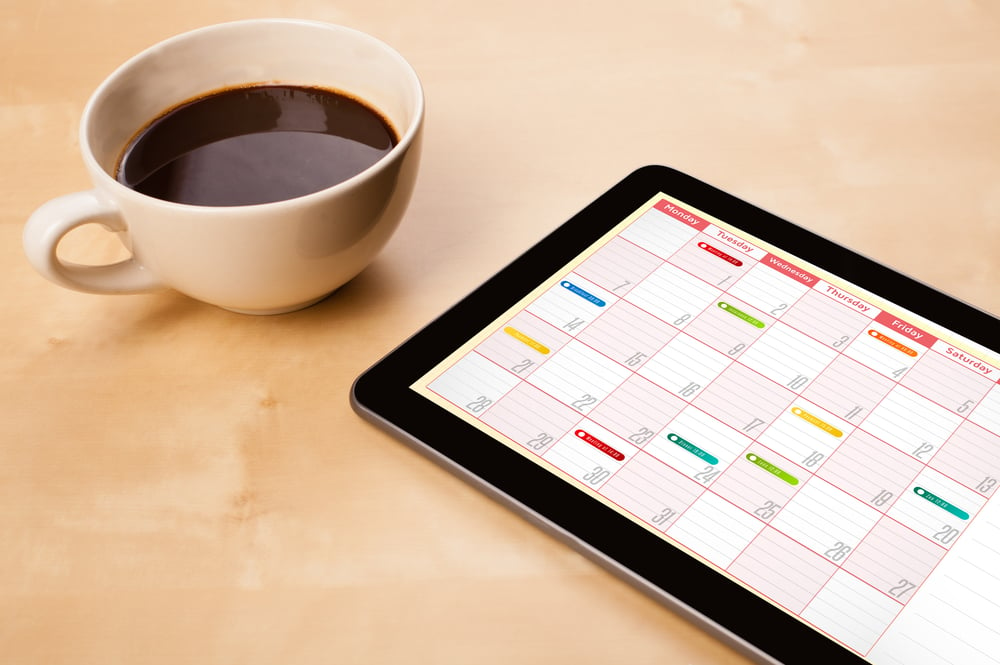 Workplace with tablet pc showing calendar and a cup of coffee on a wooden work table close-up